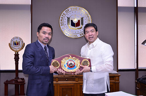 Dos hombres vestidos de gala sosteniendo un cintur&oacute;n de campe&oacute;n de boxeo frente al escudo del Senado de Filipinas.